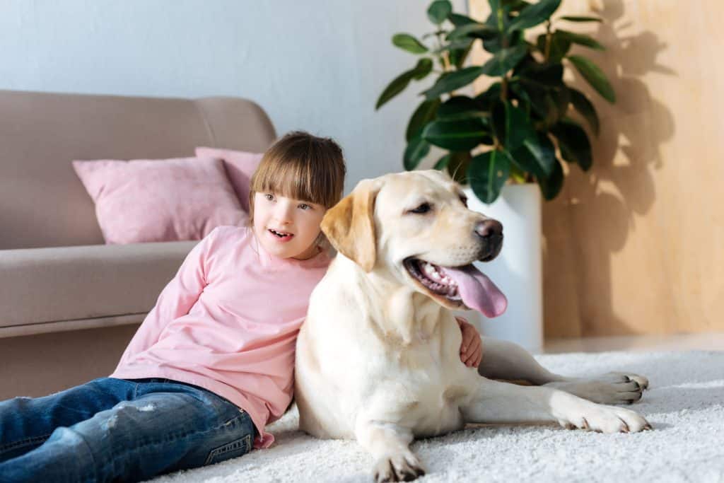 Child with down syndrome hugging Labrador retriever on the floor